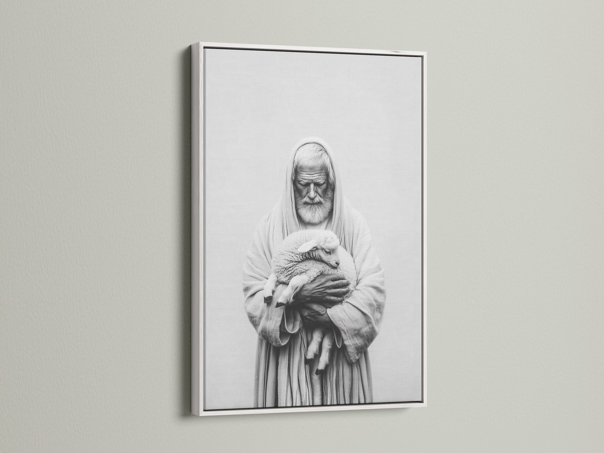 A framed artwork hangs on a light beige wall. The artwork has a white frame. The frame is thin and modern. The art print is a black and white image of a man holding a lamb. This framed art print is perfect for any room.