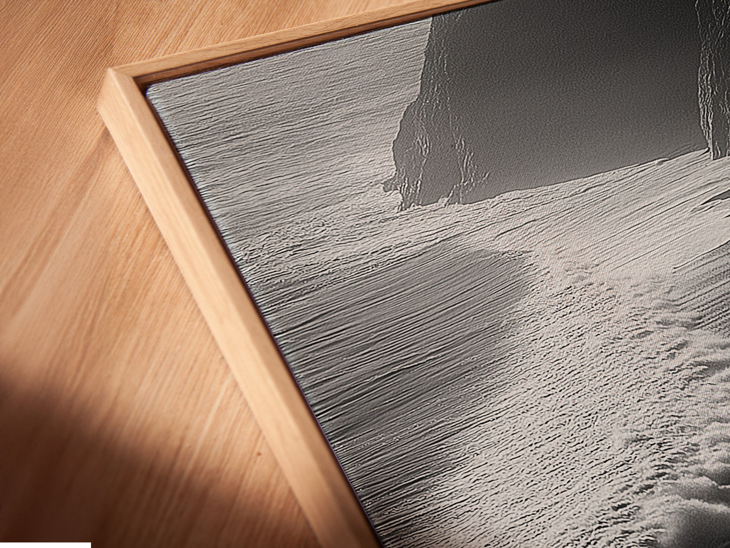 Here is a close-up of a canvas print in a floating frame. The black and white ocean waves artwork is displayed beautifully. The floating frame enhances its contemporary appeal. Ideal for modern coastal decor in any living space. This aerial beach photography captures the ocean's serene beauty. A perfect addition to elevate your home decor today.