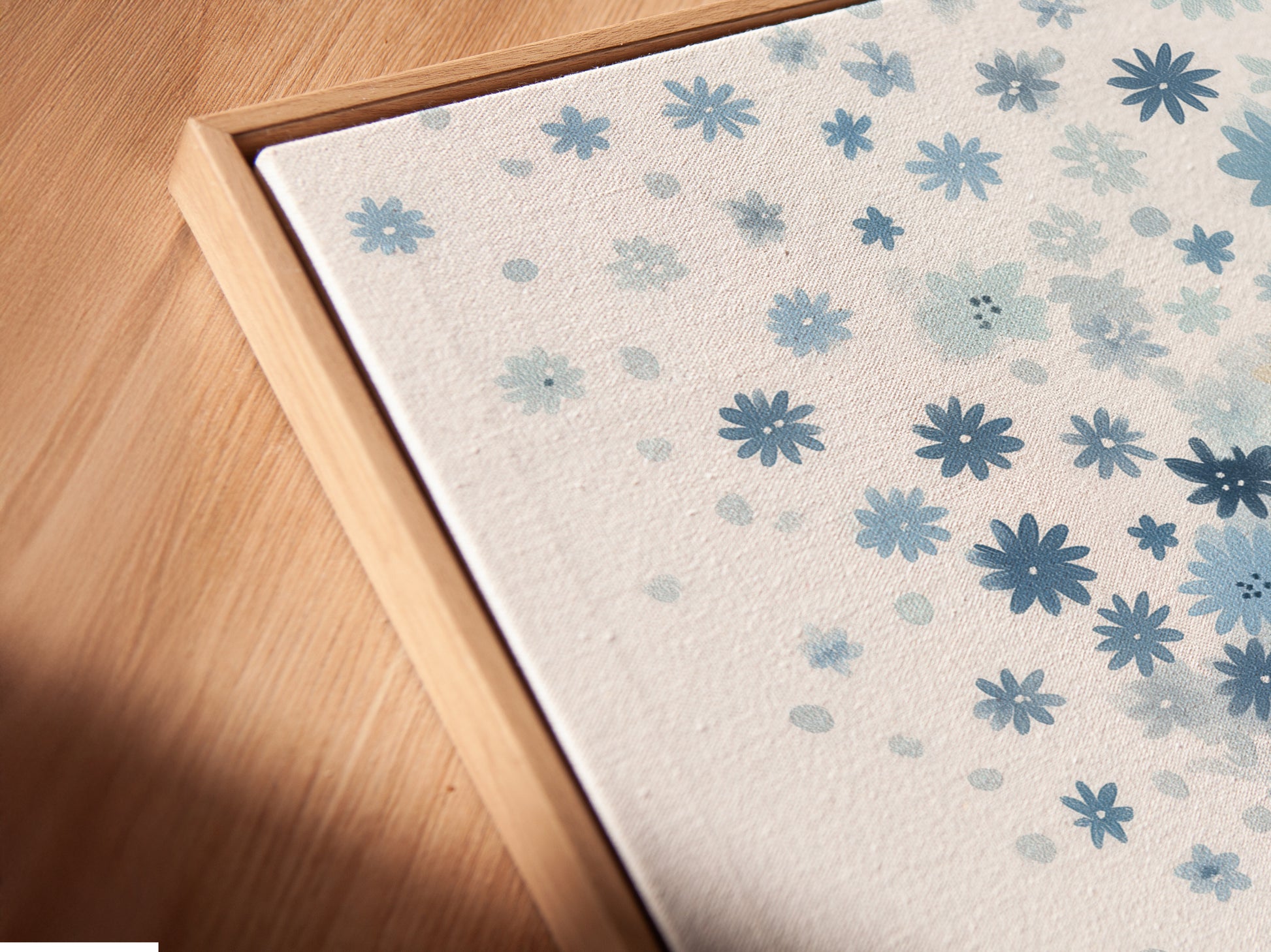 A close-up angled view of a blue floral canvas print in a floating frame. The floating frame gives the artwork a modern and airy feel. The pastel botanical art and whimsical flower tree art create a serene atmosphere. Perfect for any kids room.