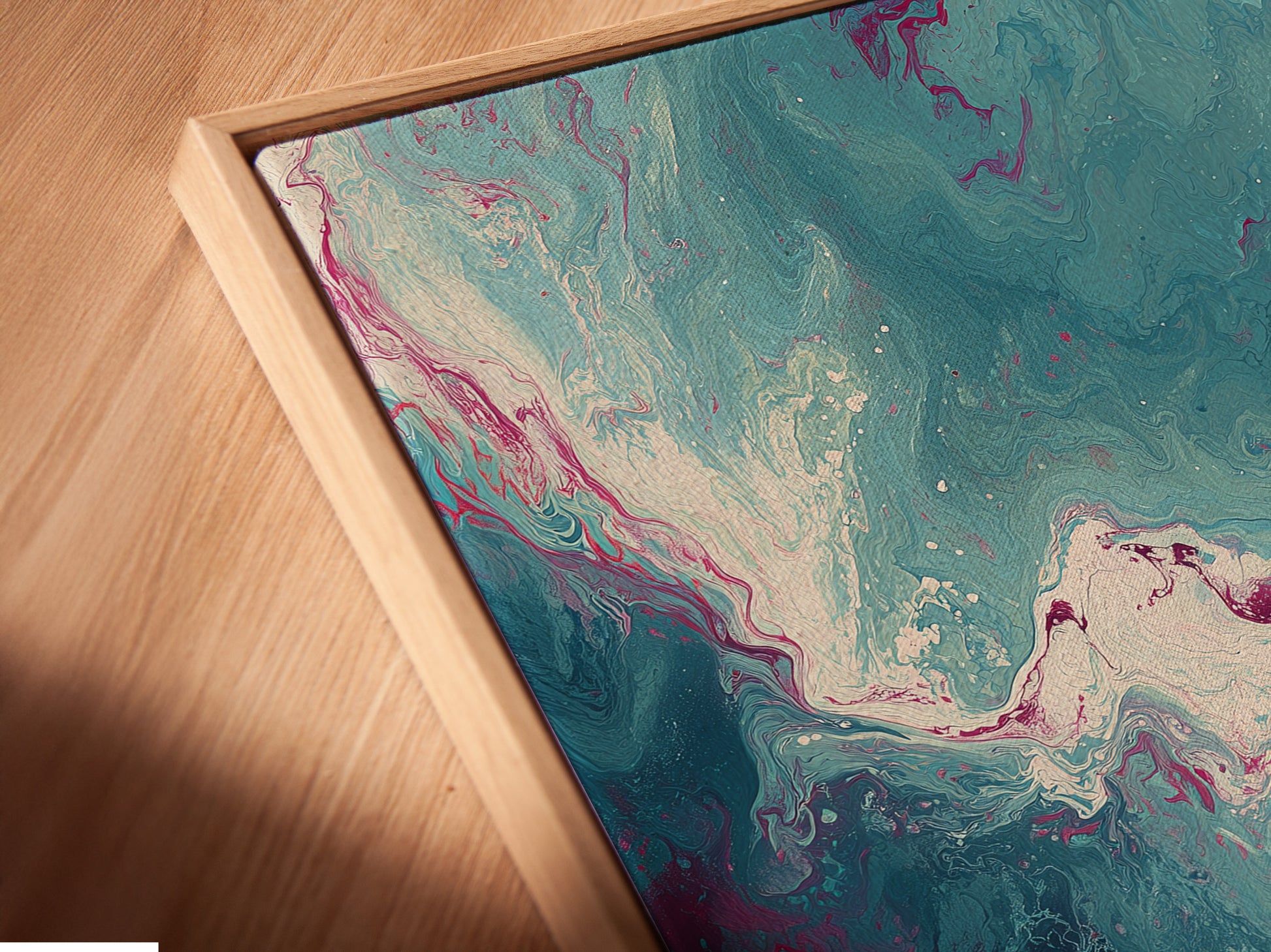 A close-up angled view reveals a canvas print in a floating frame. The abstract fluid artwork features a mesmerizing marble swirl pattern in teal and pink. The floating frame enhances the art creating a gallery-like appearance. It's perfect for modern wall decor.