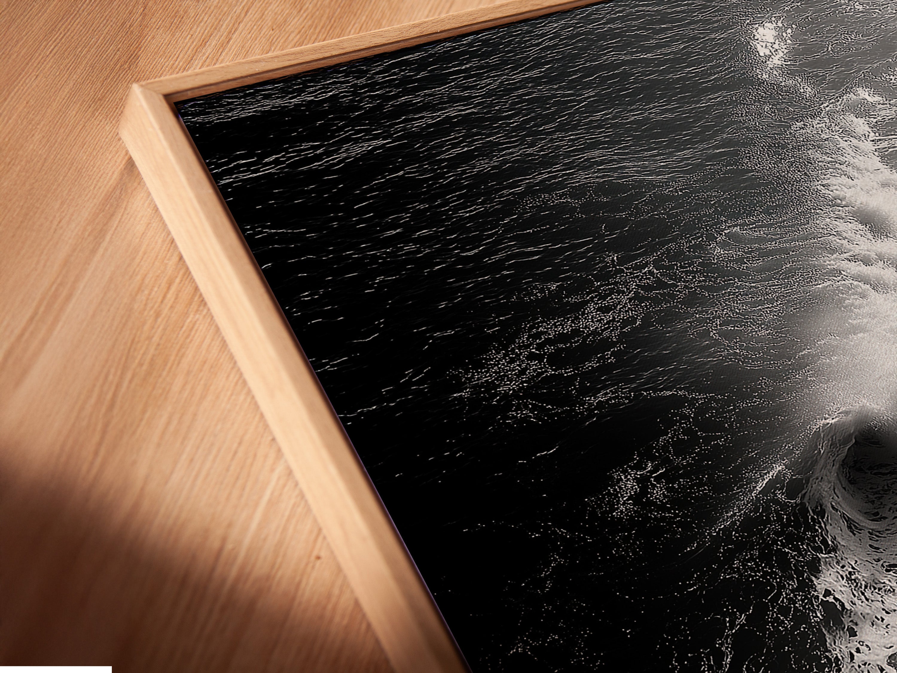 A close-up angled view reveals a canvas print in a floating frame. The artwork features a black and white ocean wave. It is perfect for minimalist decor. This beach canvas print offers a modern coastal art vibe. It is excellent for living room wall art and bedroom wall decor. Transform your space with this stunning piece.