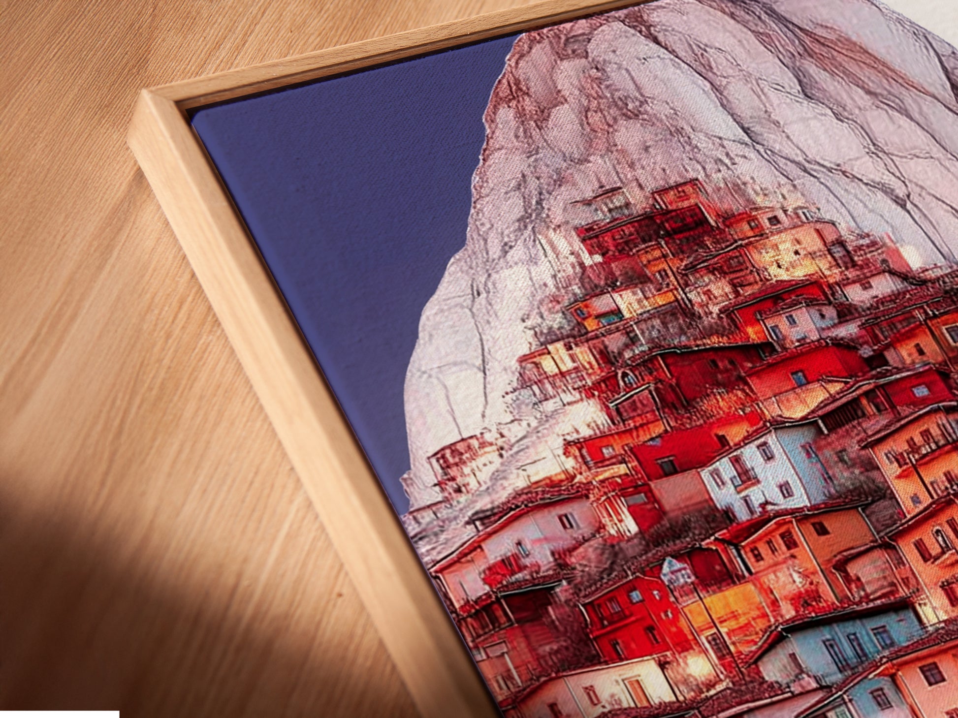 A close-up shows the Mountain Village canvas print in a floating frame. The floating frame gives a modern gallery feel to this village artwork. Perfect for showcasing coastal wall art.