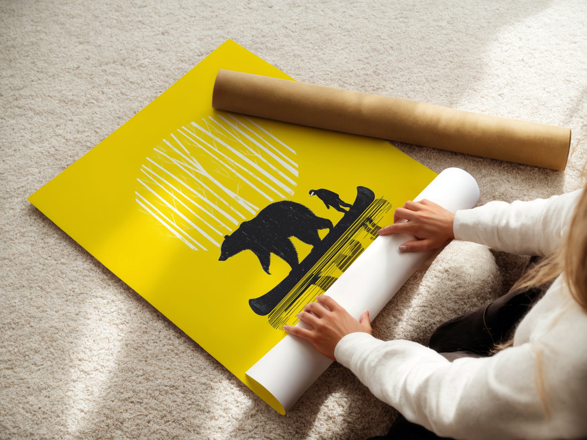 A woman is carefully rolling a fine art poster paper print of the Bear Canoe artwork. This yellow art print features a bear and man in a canoe. Perfect for forest wall art or adventure decor. Ready to be framed and displayed.