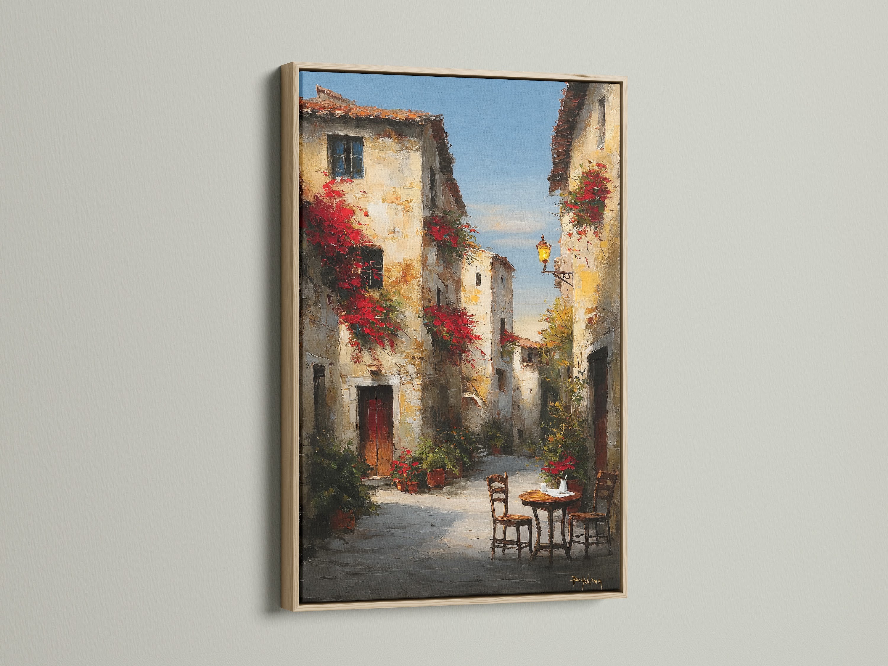 Oak frame featuring a picturesque street artwork. The artwork captures the essence of a quaint European town. Red flowers cascade from buildings. A cozy table and chairs beckon. This framed art brings warmth to any room. Discover the beauty of framed artwork.