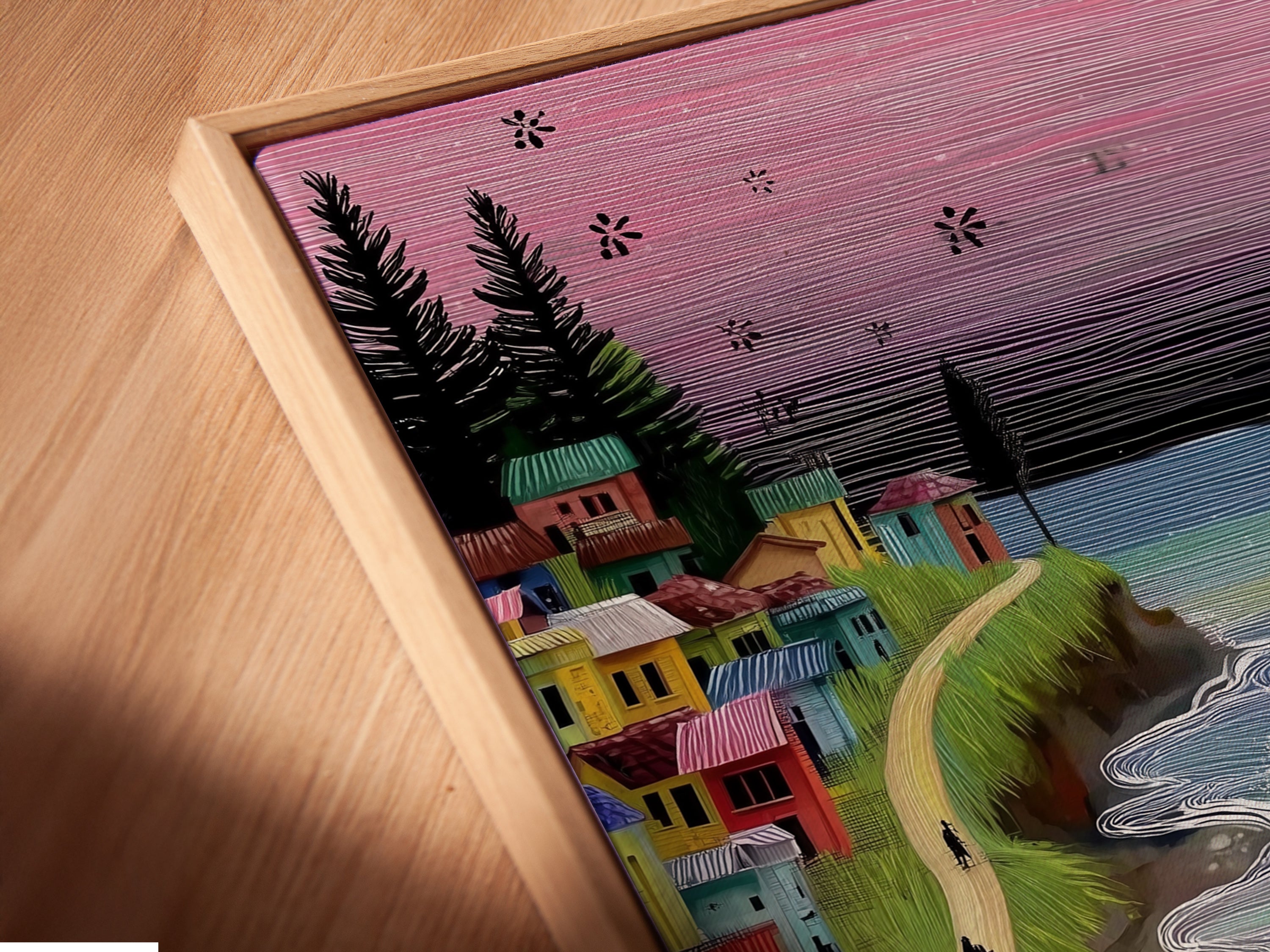 Close-up angled view of a canvas print in a floating frame. The coastal village art features a vintage van and ocean waves. The floating frame adds depth and dimension to the artwork. This whimsical seaside canvas art enhances any space. Perfect for boho beach decor.