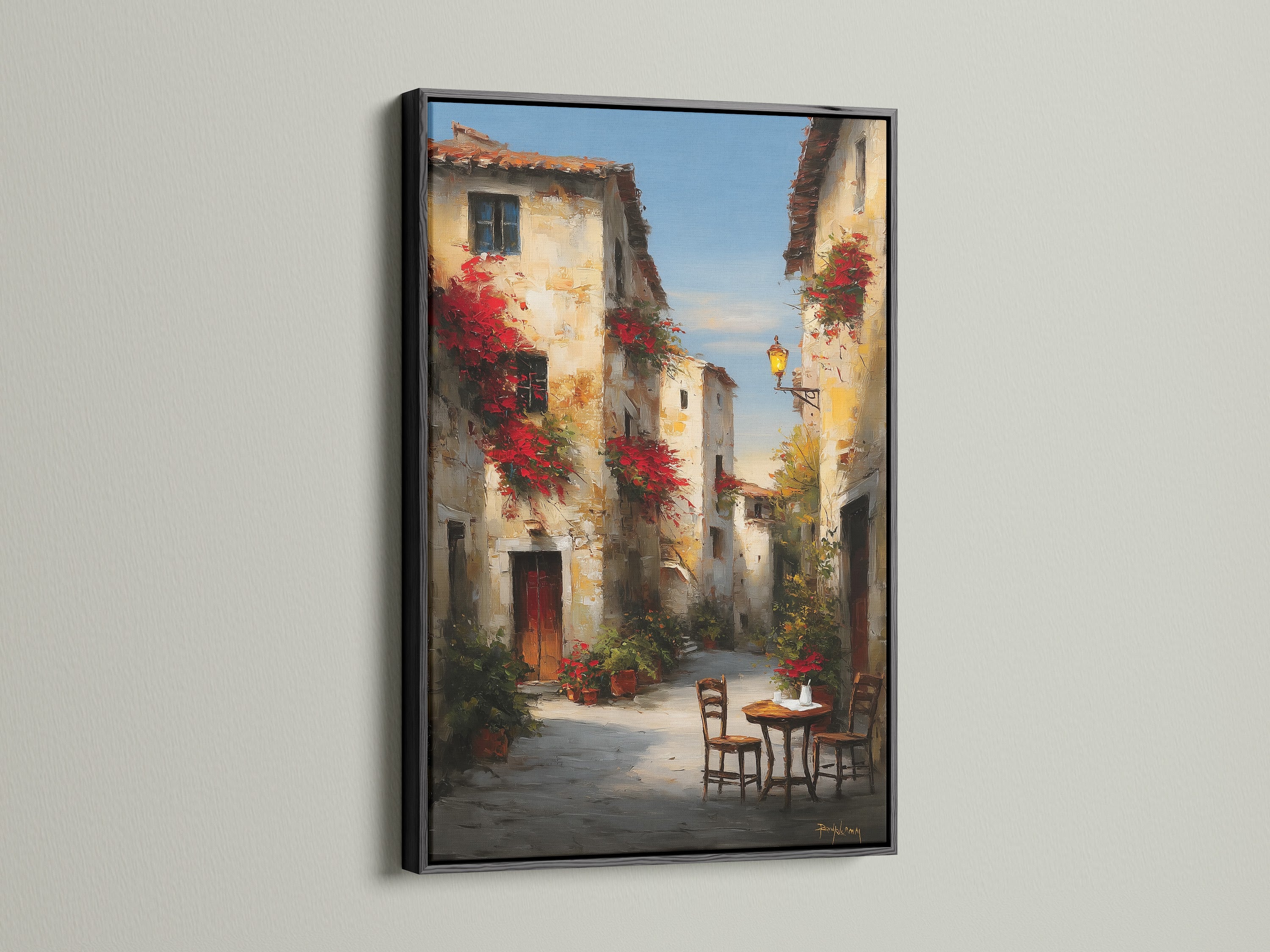 Black frame presenting a captivating street artwork. The artwork showcases a peaceful European street. Red flowers add a pop of color. A table and chairs create a welcoming scene. The black frame provides a modern touch. Elevate your decor with framed artwork.
