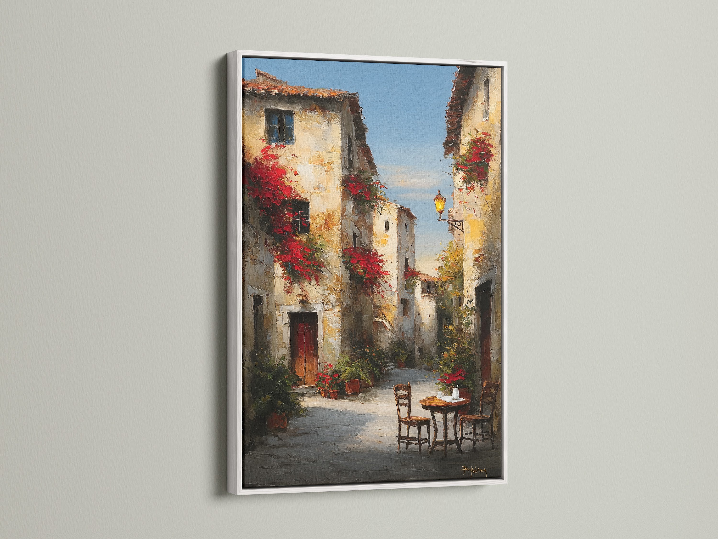 White frame displaying a beautiful street artwork. The artwork portrays a serene European street. Buildings are decorated with vibrant red flowers. A charming table and chairs invite you to relax. The white frame adds a touch of elegance. Enhance your home with stunning artwork.