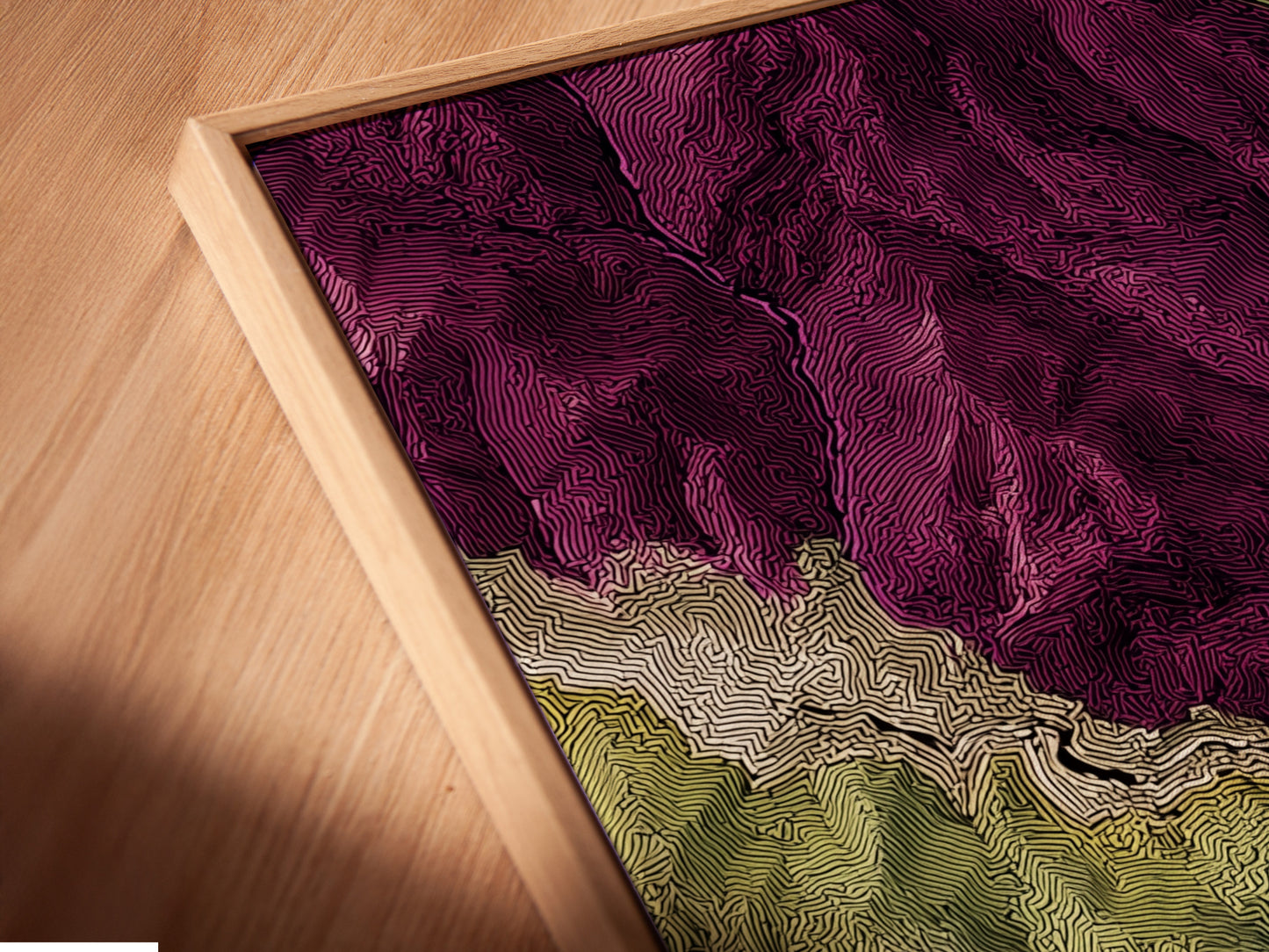 A close-up angled shot of a canvas print in a floating frame. The artwork is a topographical map. It features purple and green landscapes. The floating frame adds a modern touch. This printing method enhances the artwork. It makes the art stand out against the wall.