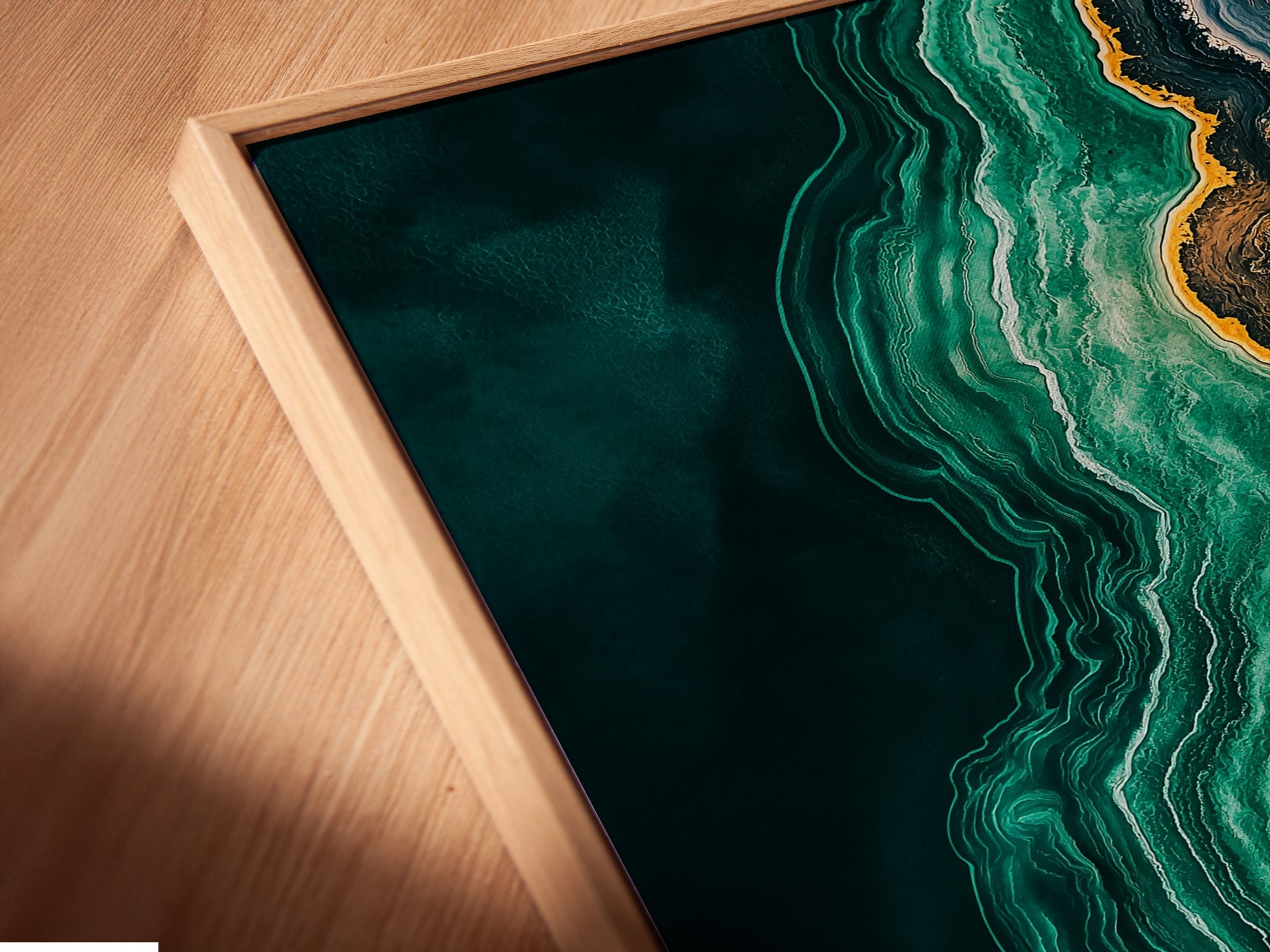 Angled close up showcasing a canvas print in a floating frame. The abstract ocean artwork features emerald green teal and gold tones. The floating frame gives a modern touch to this fluid artwork. Ideal for contemporary home decor.