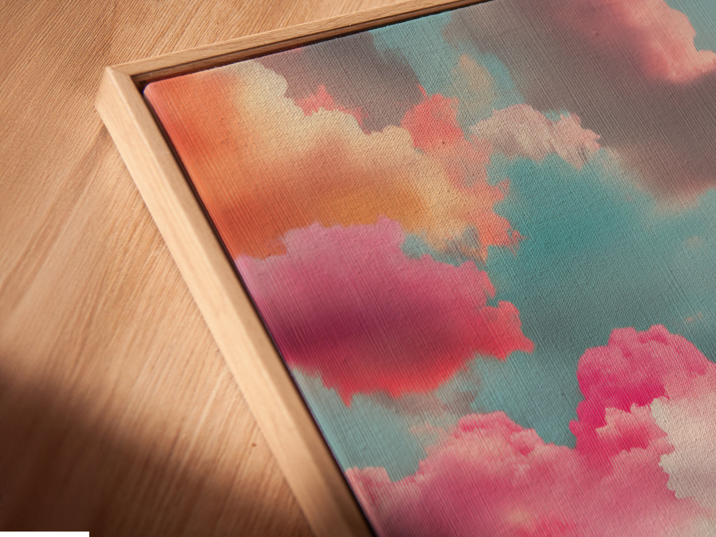 This is an angled close up of a canvas print in a floating frame. The Sunset Clouds artwork is showcased beautifully. The abstract seascape adds a modern touch. The pink clouds and teal art create a calming atmosphere. Perfect for any room.