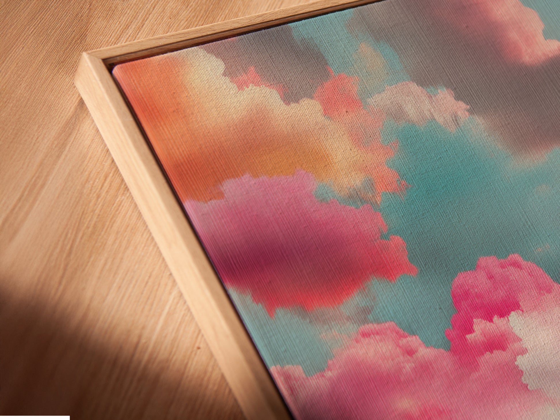 This is an angled close up of a canvas print in a floating frame. The Sunset Clouds artwork is showcased beautifully. The abstract seascape adds a modern touch. The pink clouds and teal art create a calming atmosphere. Perfect for any room.
