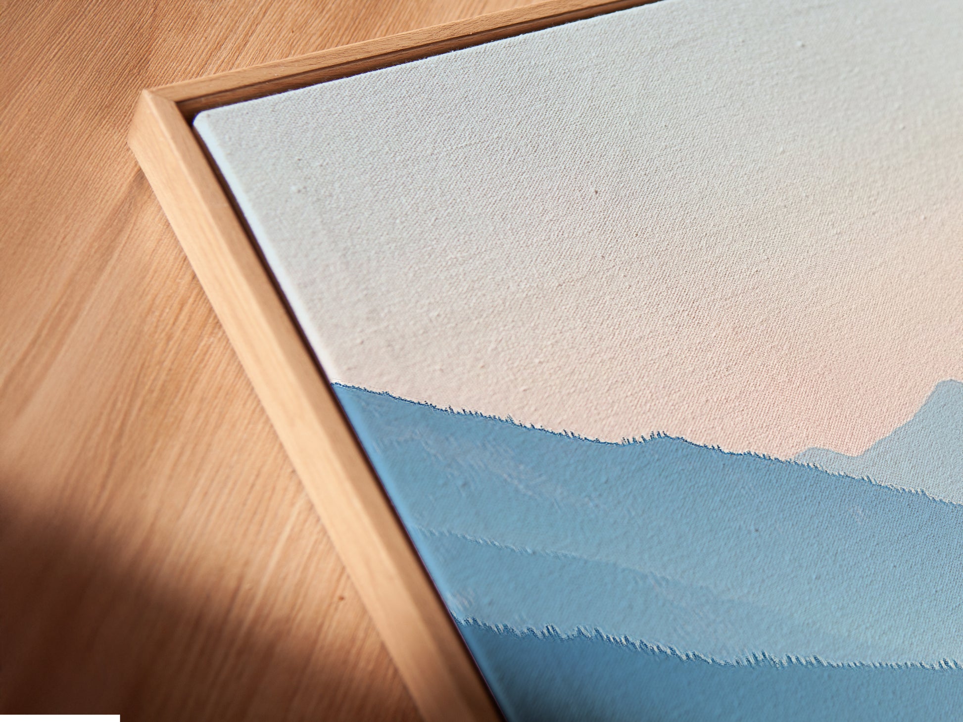 Angled close up of a canvas print in a floating frame. Pastel blue wall art is visible. The mountain lake artwork brings a serene touch. It is a calming nature landscape photography piece. Ideal for bedroom wall decor. The floating frame adds a modern touch. Enhances contemporary spaces.