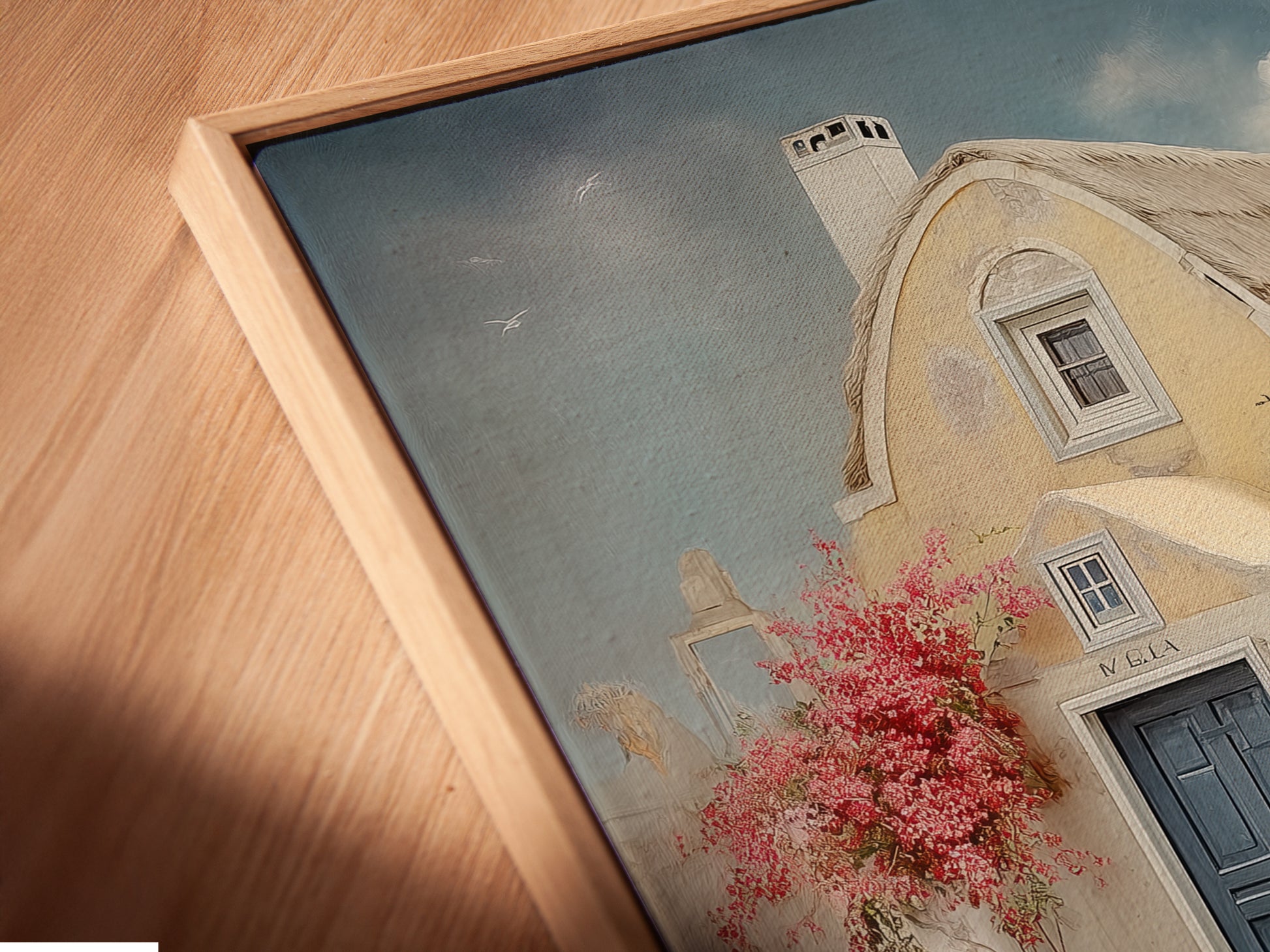 A close-up angled view of a canvas print in a floating frame. The artwork showcases a coastal house with a blue door and floral stairway. Perfect for living room wall art and bedroom wall decor. Bring Greek island art to your vacation home decor.