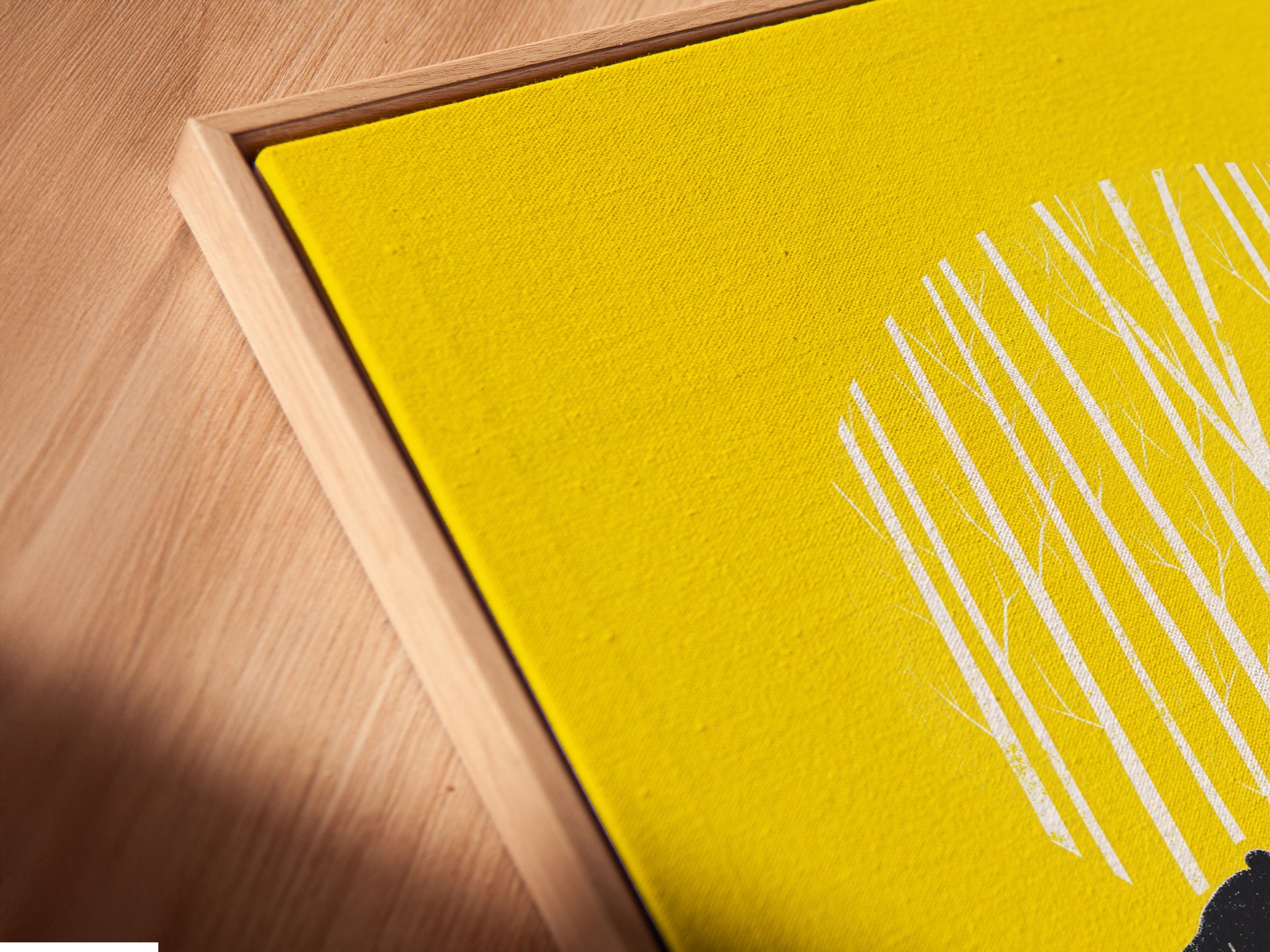 A close-up of the Bear Canoe canvas print in a floating frame. The floating frame is a great option for your nature artwork. The artwork is yellow and features a bear and man in a canoe. Great for cabin decor.