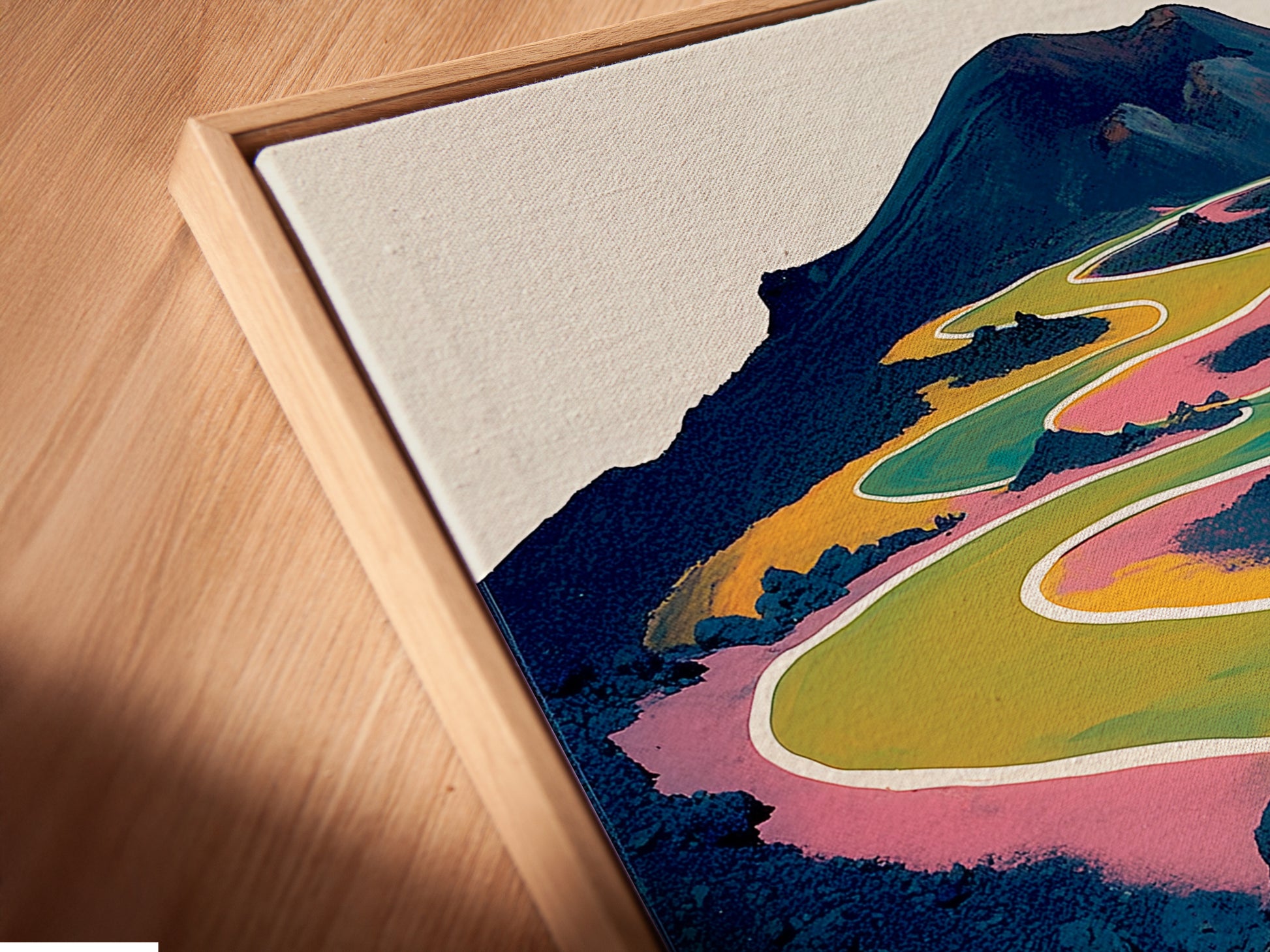 Close-up of a canvas print in a floating frame. The abstract mountain landscape artwork has a colorful winding path. The fine art is ready to elevate any room's decor.