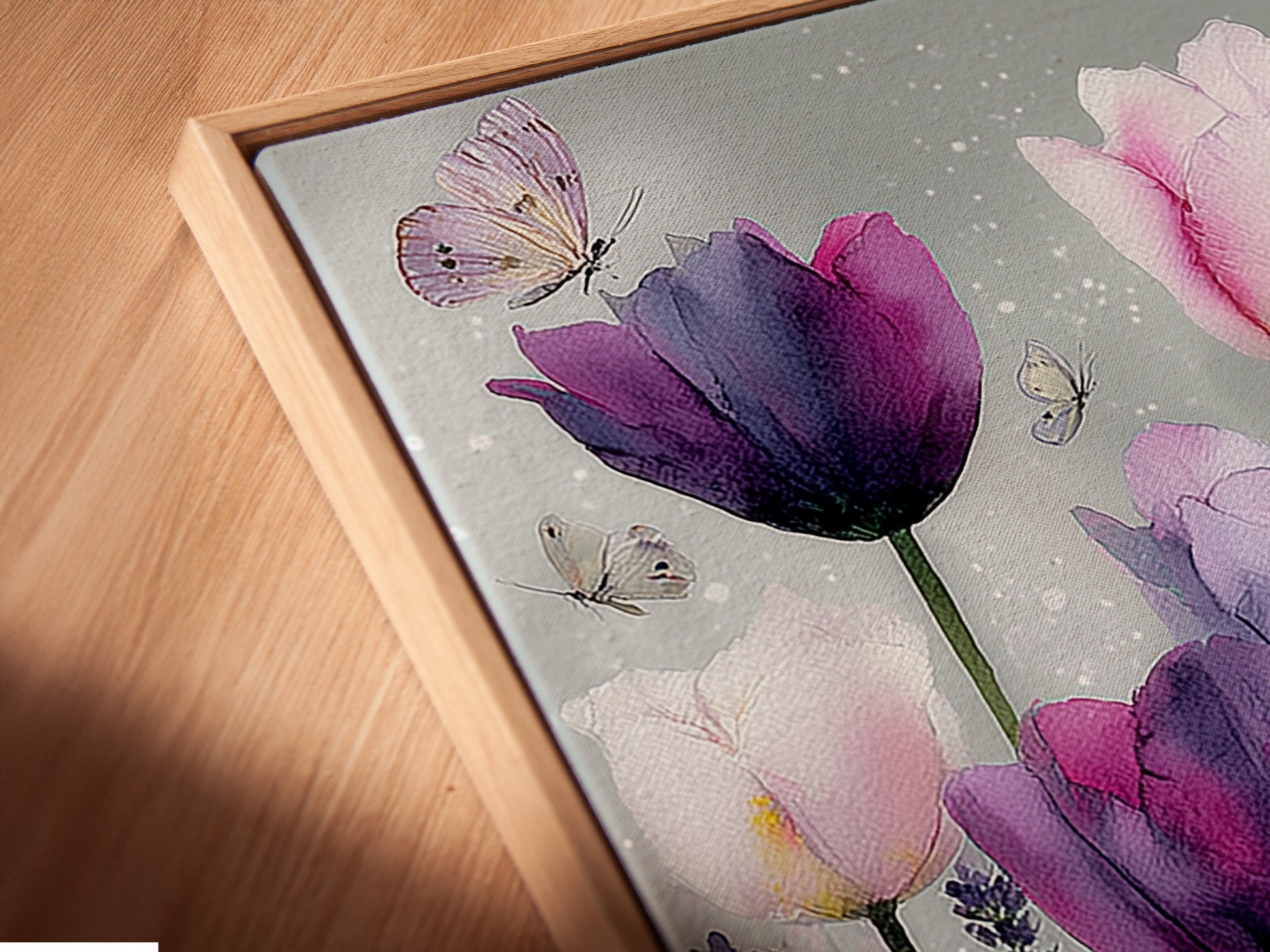 A close-up shot of a canvas print in a floating frame. The artwork features pink and purple tulips. Butterflies add a delicate touch to the floral artwork. The floating frame gives the art a modern sophisticated look. The canvas print is displayed at an angle enhancing its visual appeal.