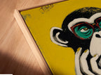 Close-up of a canvas print in a floating frame. The primate canvas art features a colorful monkey artwork. The floating frame adds a modern touch to the pop art print. The artwork is perfect for contemporary spaces. This animal wall decor is ideal for office wall art or funky home decor. The unique frame makes this piece stand out.