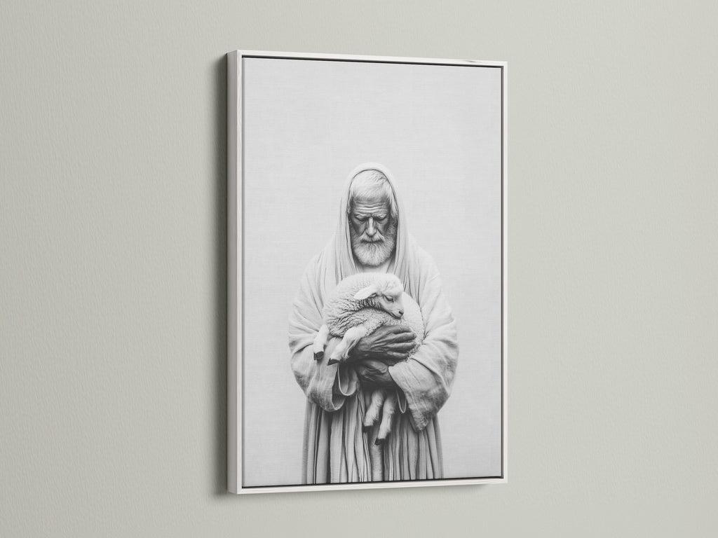 A framed artwork hangs on a light beige wall. The artwork has a white frame. The frame is thin and modern. The art print is a black and white image of a man holding a lamb. This framed art print is perfect for any room.