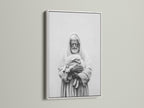 A framed artwork hangs on a light beige wall. The artwork has a white frame. The frame is thin and modern. The art print is a black and white image of a man holding a lamb. This framed art print is perfect for any room.