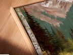 Angled close-up of a Mountain Lake canvas print in a floating frame. The artwork features a teal lake surrounded by a forest and mountains. The floating frame enhances the artwork's modern appeal. Perfect for adding a touch of woodland elegance to any living space. Bring nature indoors.