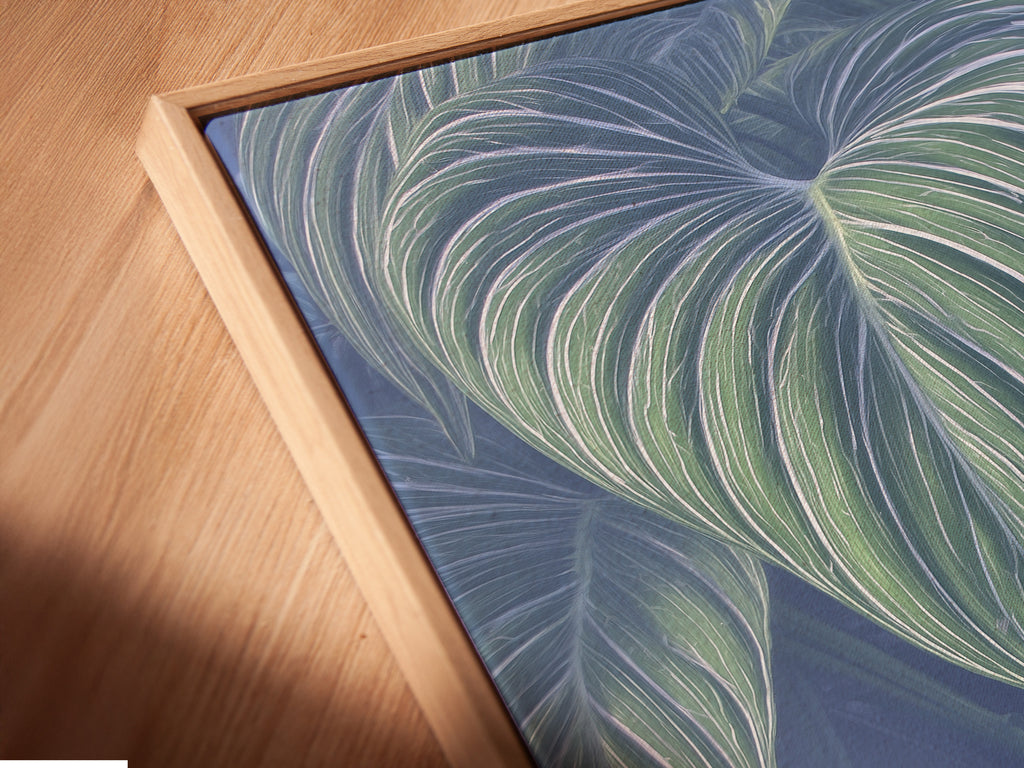 A close-up shows a canvas print in a floating frame. The tropical leaf art appears modern. The blue green colors are vibrant. This is perfect for contemporary wall art. See the detail in this canvas.