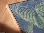 A close-up shows a canvas print in a floating frame. The tropical leaf art appears modern. The blue green colors are vibrant. This is perfect for contemporary wall art. See the detail in this canvas.