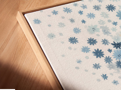 A close-up angled view of a blue floral canvas print in a floating frame. The floating frame gives the artwork a modern and airy feel. The pastel botanical art and whimsical flower tree art create a serene atmosphere. Perfect for any kids room.