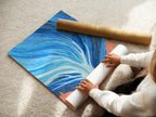 A woman carefully rolling a fine art poster paper. The poster features the Abstract Tree artwork. This blue and coral wall art is perfect for modern decor. It is ideal for art enthusiasts seeking unique pieces. The fine art paper ensures a high quality print.