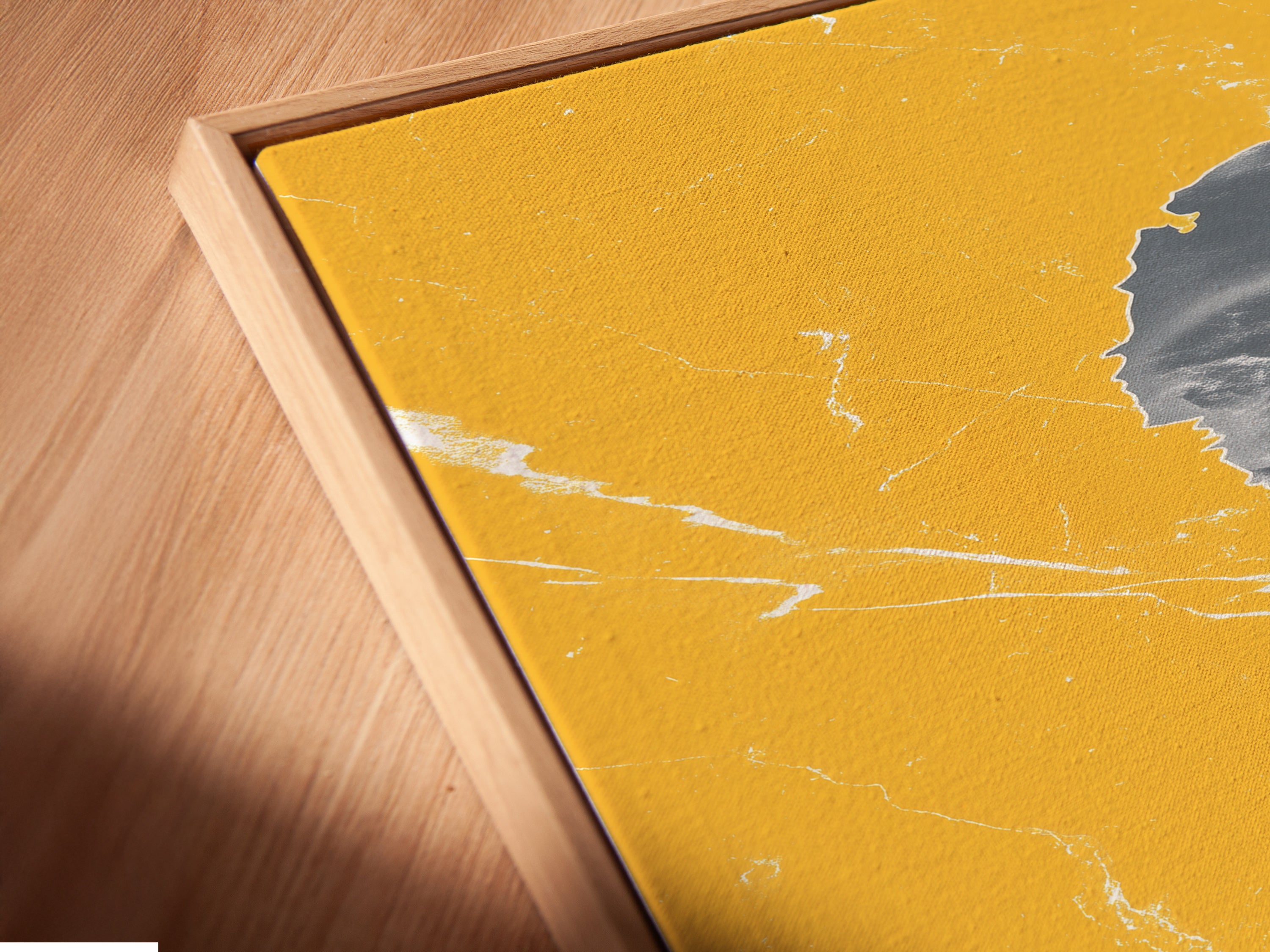 Close-up angled view of a canvas print in a floating frame. The abstract coastline artwork features mustard yellow and gray tones. This modern seascape art piece is perfect for adding a stylish touch to your home decor.