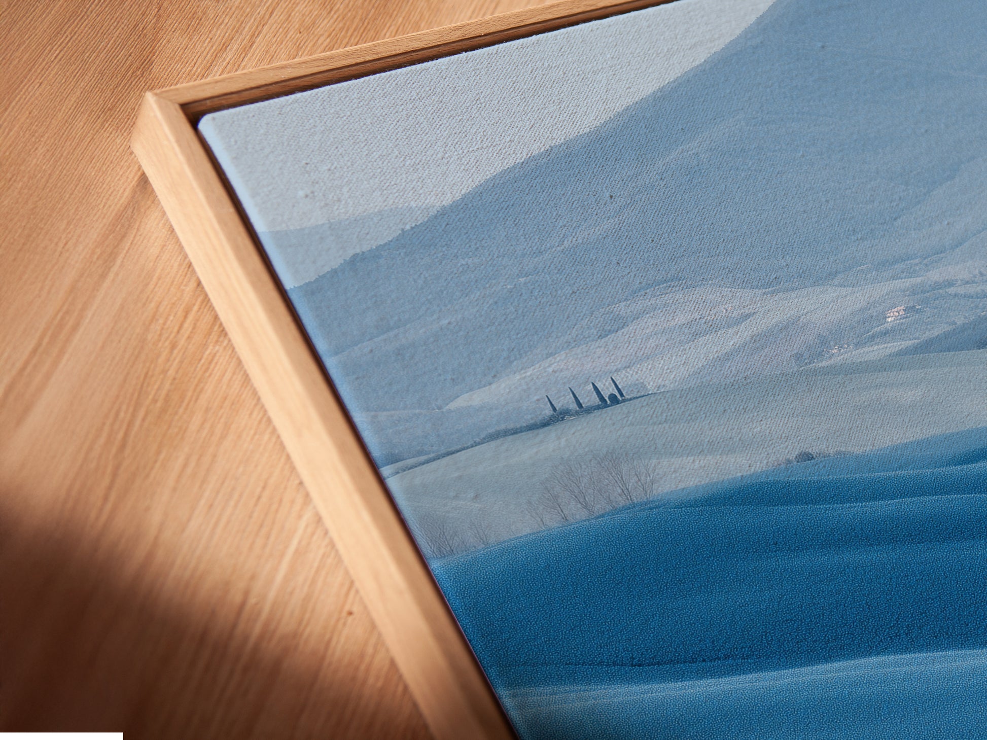 Close up of a Tuscan Landscape canvas print in a floating frame. The floating frame gives the artwork a modern gallery look. The rolling hills and farmhouse scenery are highlighted. This fine art print is perfect for adding depth to your wall decor. A stylish choice for home decor.