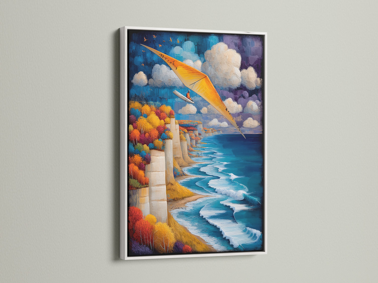 Coastal Cliff Wall Art in a white frame. Aviation artwork enhances any living space. The artwork features a seascape view. Notice the blue ocean and cliffside scenery. Add adventure to your walls with this hang gliding art print. Great for homeowners and renters.