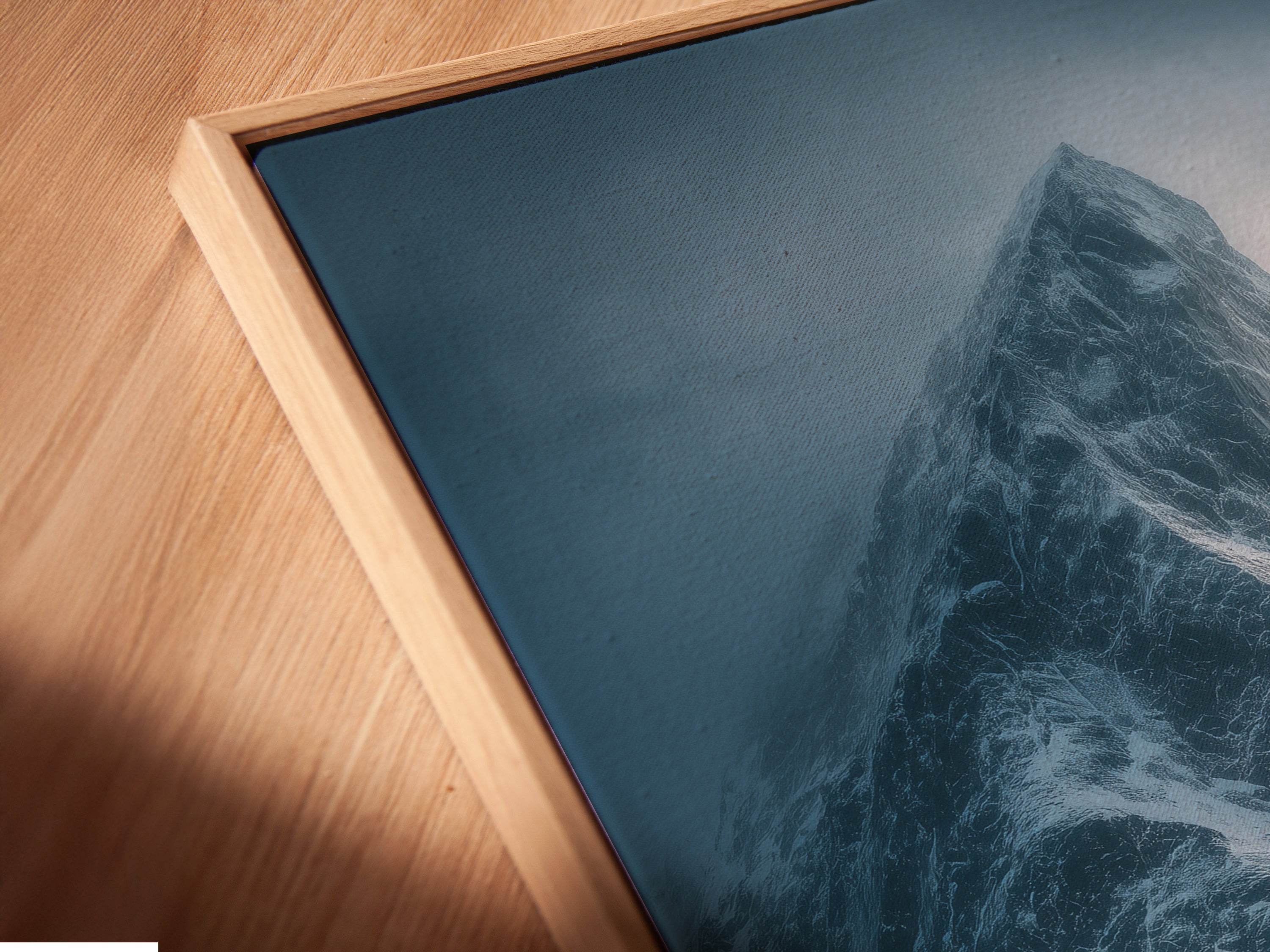 Close-up of a canvas print in a floating frame. This mountain art features a snowy landscape. The moody blue photography adds a contemporary touch. Ideal for modern wall art in any room.