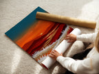 A woman is carefully rolling a fine art poster paper featuring a mountain sunset. The warm orange and teal landscape is printed on high-quality paper. This poster paper allows for versatile framing options. It is ideal for those who enjoy changing their wall art frequently. Great for bedroom wall decor.