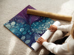 A woman carefully rolling a fine art poster paper. She's preparing it for framing or display. The poster features abstract fluid art in purple and teal tones. This high-quality print is perfect for modern wall decor. It is available in various sizes to suit your needs.