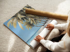 A woman is carefully rolling a fine art poster paper print. The print features a tropical beach scene. This high-quality poster is perfect for adding a coastal touch to any space. Frame it or hang it as is.