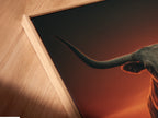 Close-up of a longhorn bull canvas print in a floating frame. The artwork features a dramatic sunset. The floating frame gives it a modern gallery look. Perfect for adding a touch of western charm to your home. Great cowboy wall decor.