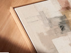A close-up angled view shows a canvas print in a floating frame. The abstract artwork has neutral blush pink and gray tones. This modern minimalist print is great for bedroom wall decor. The floating frame adds a contemporary touch. Perfect for a modern living space.