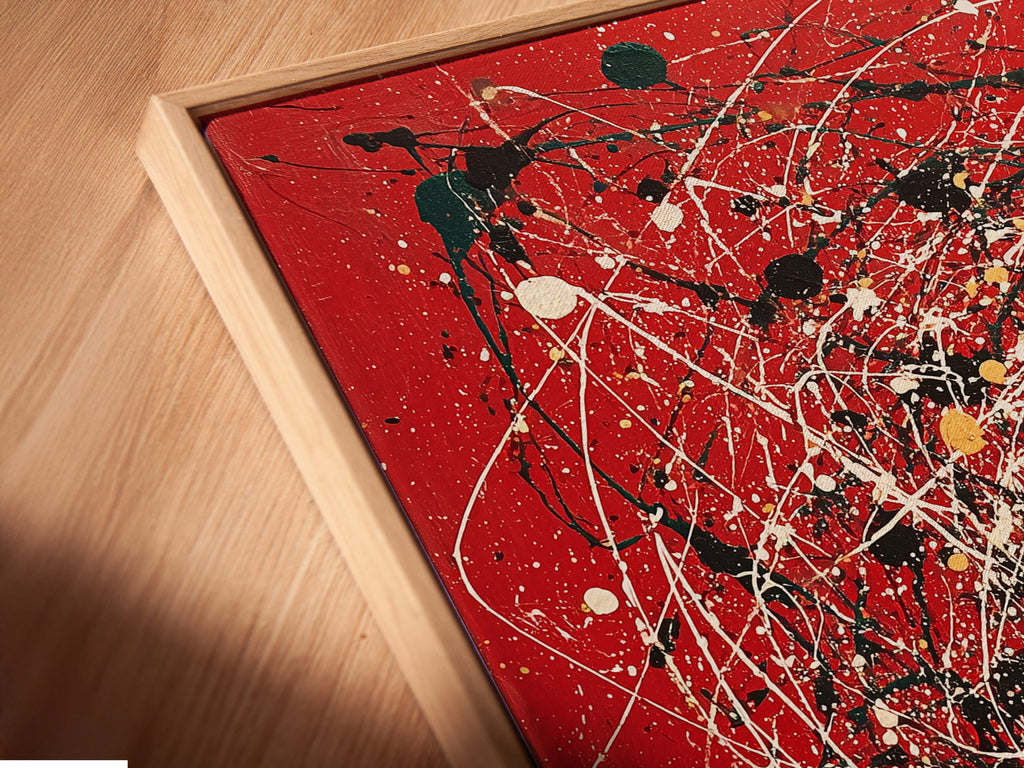 A close-up angled view of a canvas print in a floating frame. The abstract artwork features red canvas with splatter art. Paint drips add a modern and contemporary touch. This piece enhances any home decor. Ideal for those seeking unique and stylish wall art. Perfect for living rooms and offices.