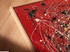 A close-up angled view of a canvas print in a floating frame. The abstract artwork features red canvas with splatter art. Paint drips add a modern and contemporary touch. This piece enhances any home decor. Ideal for those seeking unique and stylish wall art. Perfect for living rooms and offices.