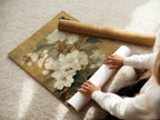 A woman carefully rolling a fine art poster paper. Preparing a vintage botanical print for framing. High-quality materials ensure a lasting piece of art. The poster paper showcases the intricate details of the white flowers and butterfly artwork. Perfect art for minimalist spaces.