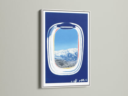Artwork featuring an airplane window view in a white frame. The art displays a beautiful mountain landscape with a clear blue sky. A modern print perfect for adding vacation vibes to any room. A great travel gift idea.