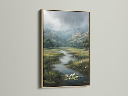 An oak frame surrounds a beautiful landscape artwork. The piece features a serene river flowing through a lush green valley. Distant mountains are shrouded in mist. The frame enhances the artwork's natural tones. It creates a cohesive and calming aesthetic on the white wall.