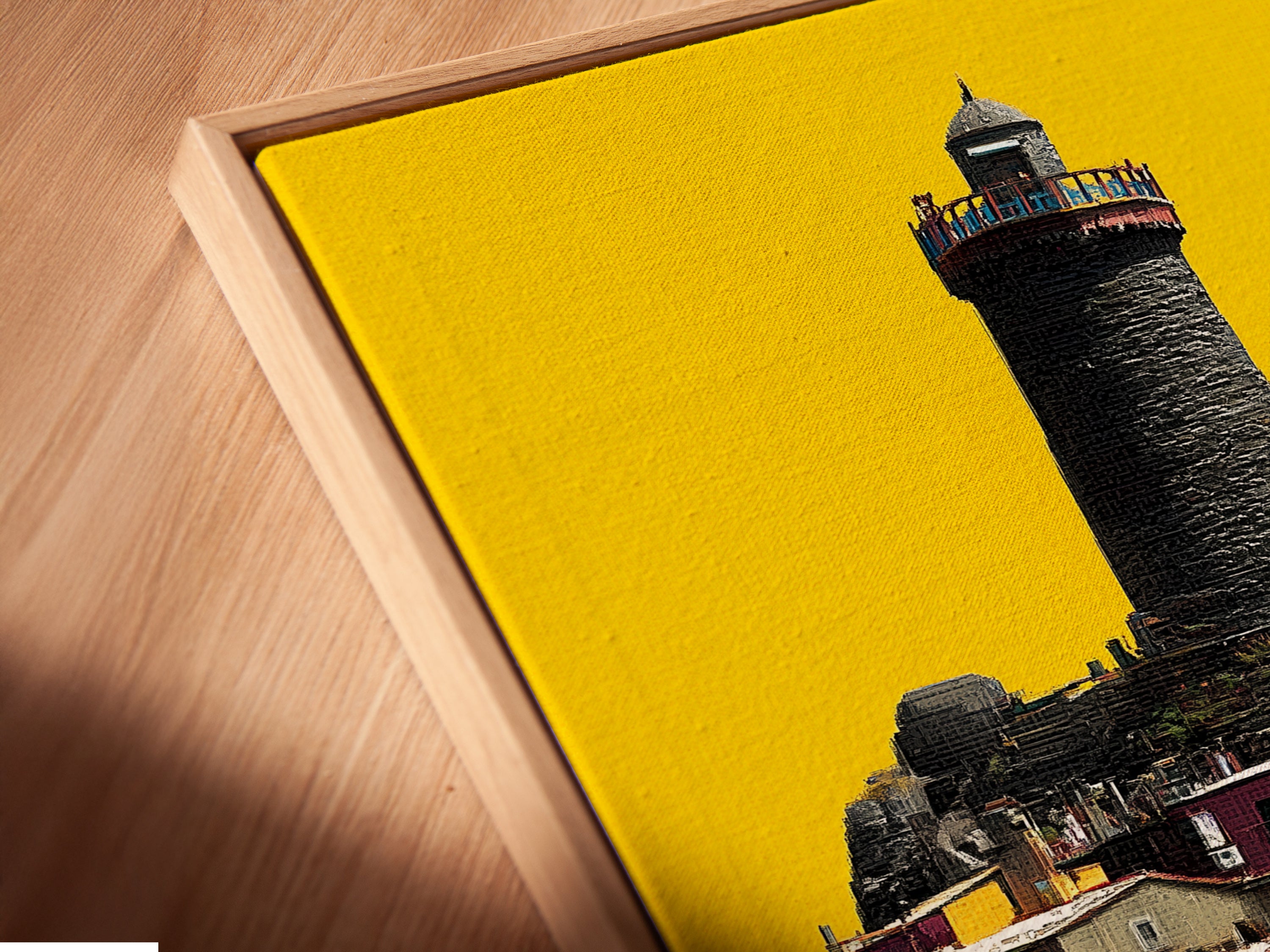 A close-up of a canvas print in a floating frame. The artwork shows a coastal village with a lighthouse. The floating frame gives a modern look. This piece is perfect for adding color and charm to any interior setting.