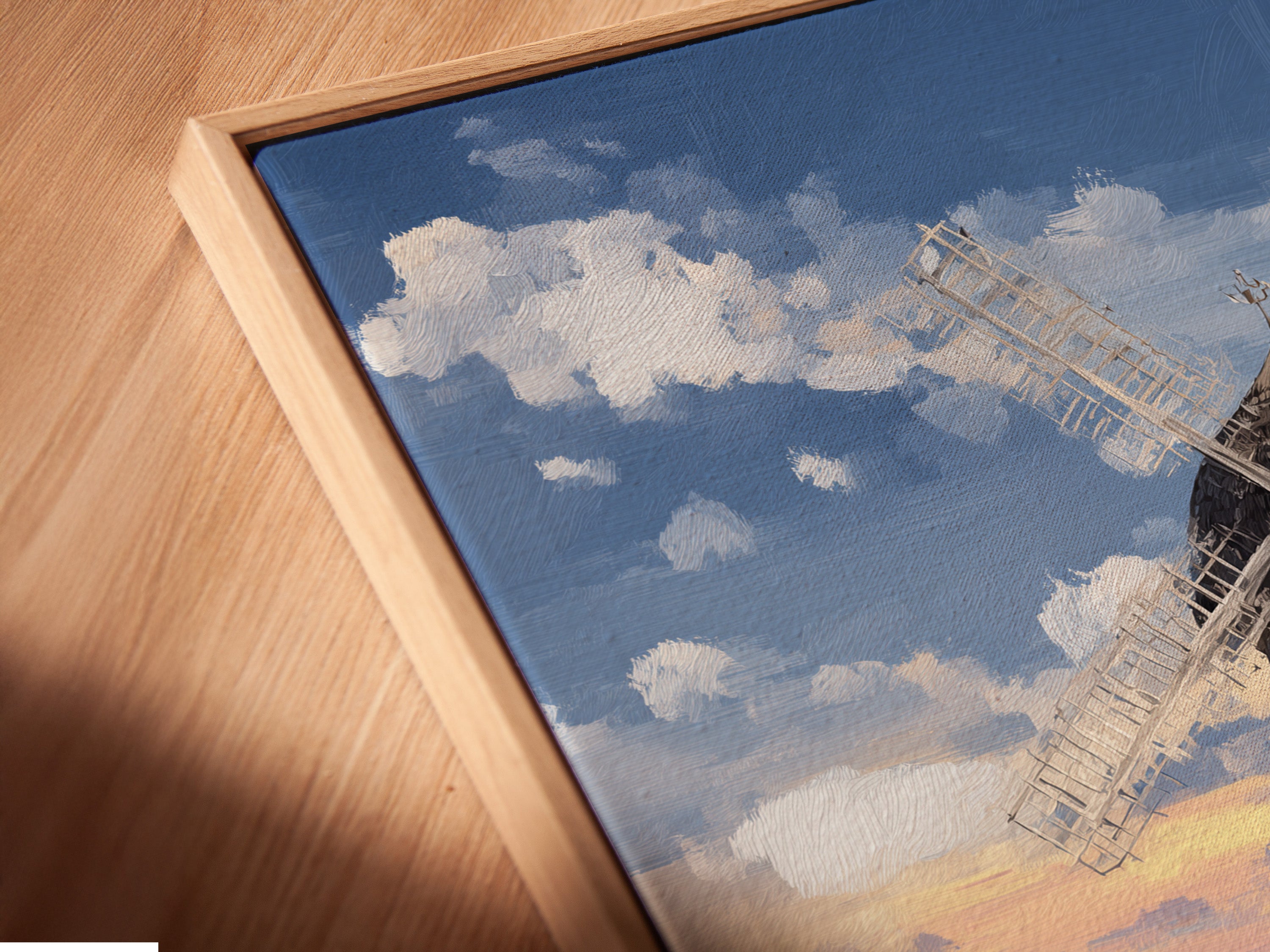 An angled close up shows a canvas print in a floating frame. The artwork depicts a coastal countryside scene with a windmill. This modern framing style adds depth and dimension to your wall art. Perfect for showcasing fine art this piece brings vintage farmhouse charm and seaside tranquility to your space.