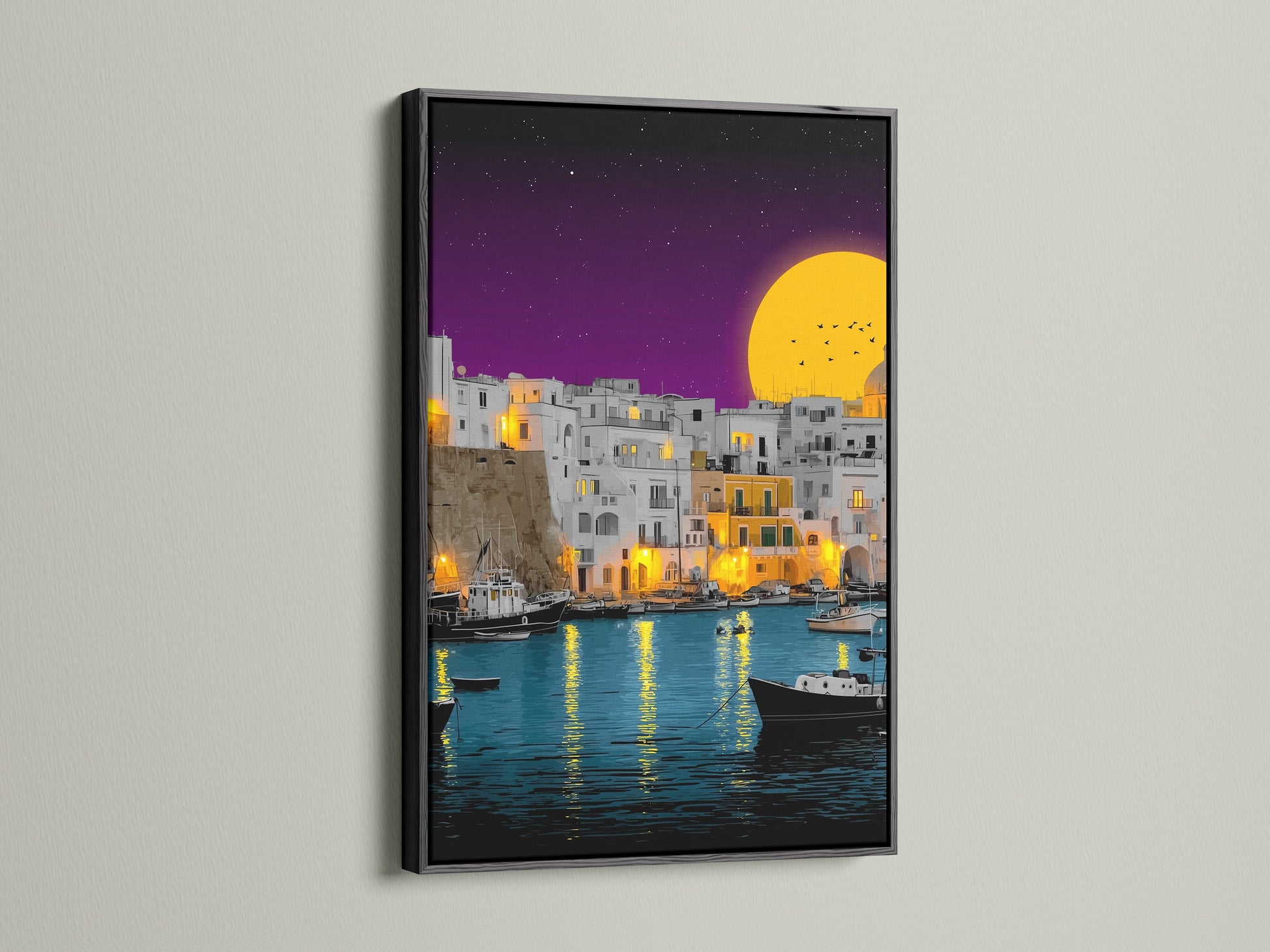 The black frame provides a striking contrast to the coastal village artwork. The artwork portrays a vibrant Mediterranean harbor scene. The harbor is filled with boats and illuminated buildings. It is a stunning piece of evening wall art.