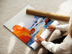 A woman is carefully rolling a fine art poster paper. This poster features a coastal seascape artwork with orange and blue tones. This modern beach landscape is printed on high quality paper. Ideal for framing or displaying as is. Coastal art for your home.