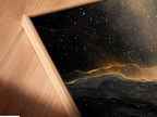 A close up of a canvas print in a floating frame. The art is abstract black and gold. The floating frame gives the art a modern look. It creates a shadow effect. The canvas print adds texture to the artwork. This is a stylish piece for any home.