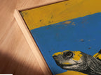 Close-up angled view of a canvas print in a floating frame. The artwork features a turtle wearing sneakers. This animal wall art adds a contemporary quirky touch to any room. Perfect for those seeking unique office decor. The art print features yellow and blue.