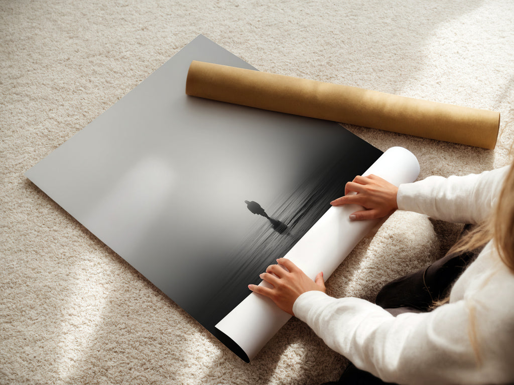 A woman is carefully rolling a fine art poster paper. This is a minimalist solitude artwork. The black and white photography captures a foggy water reflection. Perfect for art collectors.
