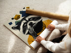 A woman is carefully rolling a fine art poster paper. The raccoon art print is perfect for adding a touch of whimsy to any space. This whimsical animal wall art is ideal for kids room decor. Fine art poster paper ensures high-quality reproduction of the playful animal portrait art. The mustard yellow geometric design is eye-catching.